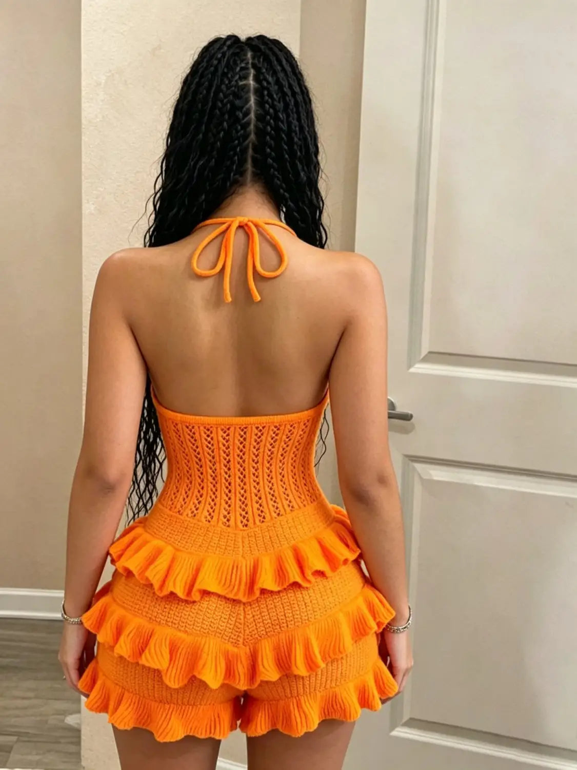 A vibrant orange knitted ruffle halter romper summer playsuit featuring a corset-style top with tied-back neck and layered ruffle shorts.