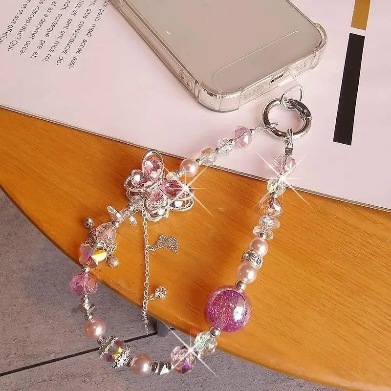 Une délicate chaîne pour téléphone mobile à thème papillon rose et argent, ornée de perles étincelantes, de perles et d’une sphère violette scintillante.