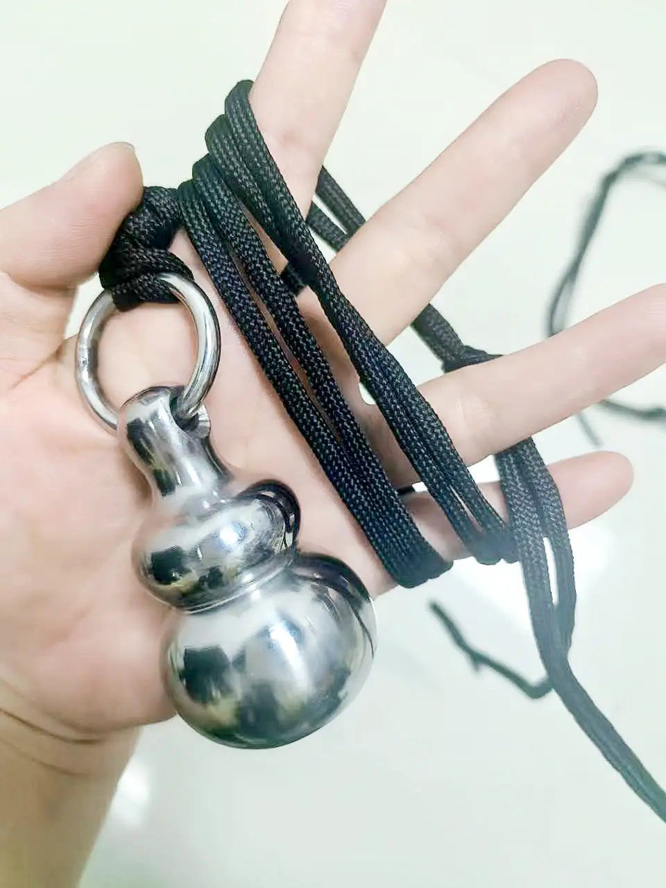Silver-toned brass gourd self defense pendant necklace suspended from a black braided cord.