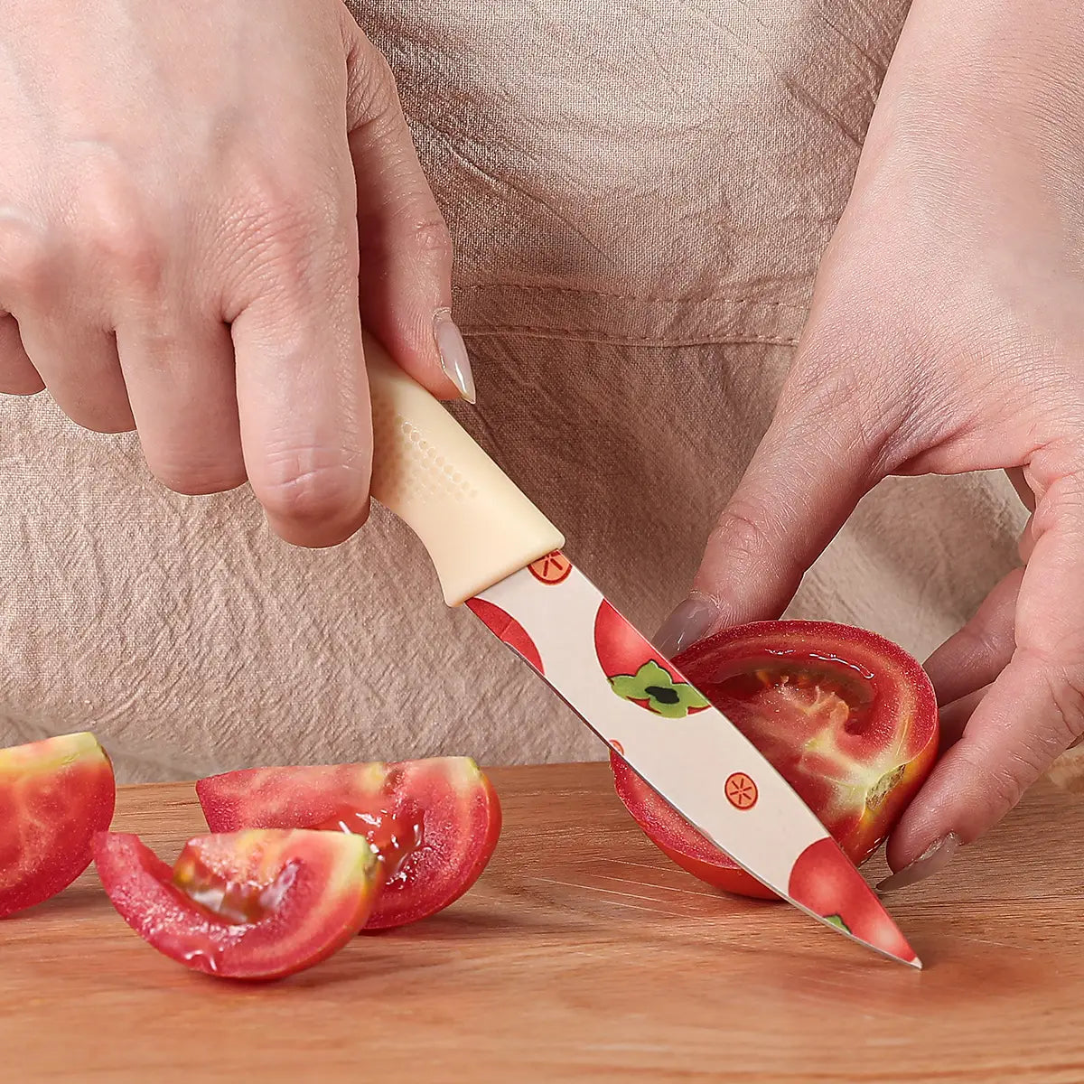 A ceramic kitchen knife with a beige handle and a white blade featuring a red tomato and green leaf pattern.