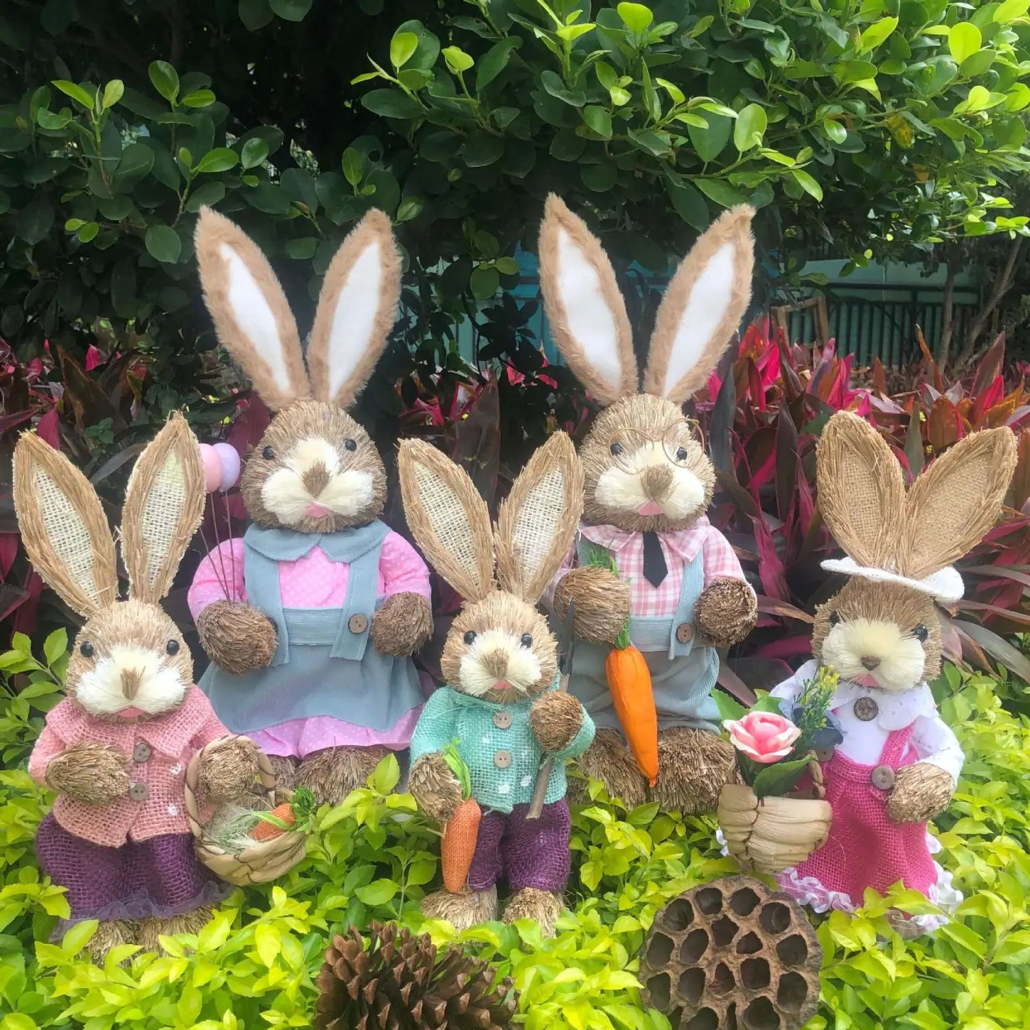 A family of five handmade straw Easter rabbit figurines each 35cm tall dressed in colorful woven outfits with button details holding carrots or flowers.