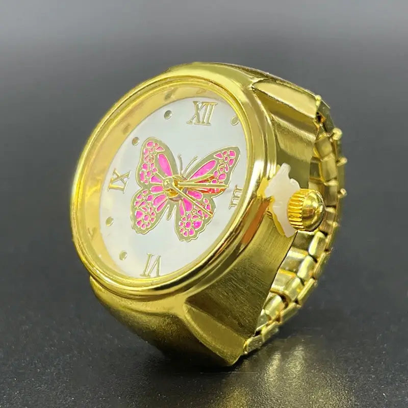 Gold-toned stainless steel ring-style watch featuring a white face with roman numerals and an ornate pink butterfly design, presented as cute jewelry.