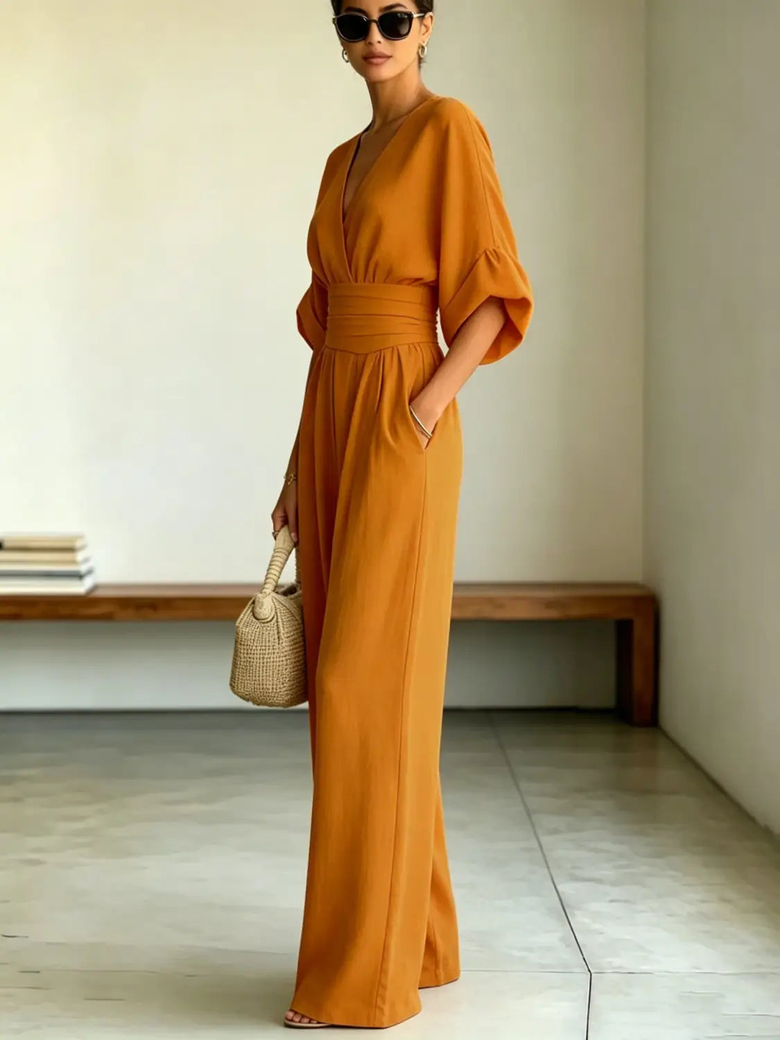 A flowing orange wide-leg jumpsuit with a v-neckline, cinched waistband, and bell sleeves made from lightweight fabric.