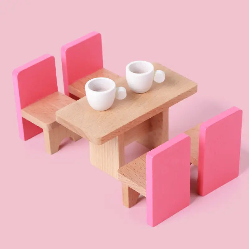 Miniatur-Holztisch mit rosa gepolsterten Stühlen und zwei weißen Porzellantassen aus einem Holz-Puppenhaus-Möbelset für Kinder als Miniaturspielzeug.