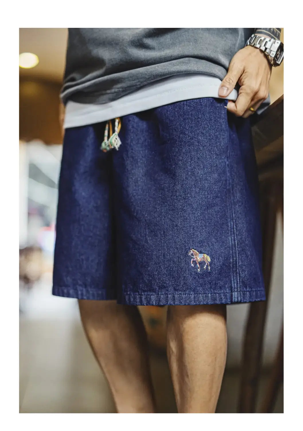Dunkelblaue Jeansshorts für Herren mit einer kleinen bestickten Pferdeapplikation am unteren Bein im Vintage-Stil.