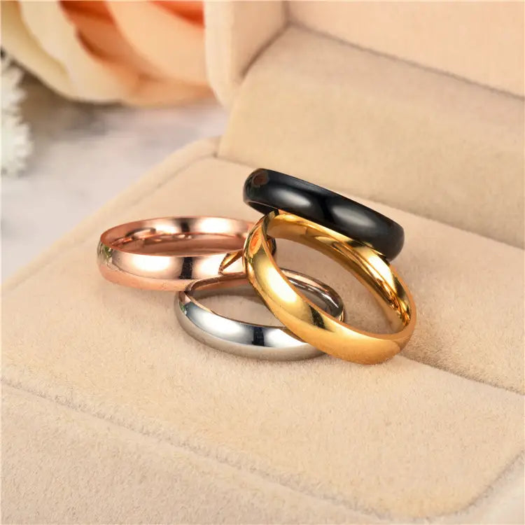 Set of four sleek polished stainless steel wedding bands in rose gold yellow gold silver and black onyx finishes.