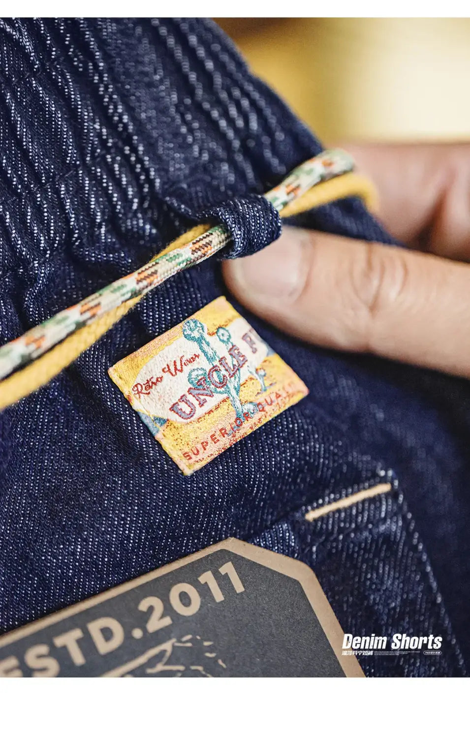 Vintage bestickte Jeansshorts für Herren mit einem Vintage-Style Webetikett mit Uncle-t-Markierung und farbenfrohem Retro-Design, auf dunkelblaue Denim-Jeans aufgesteppt.