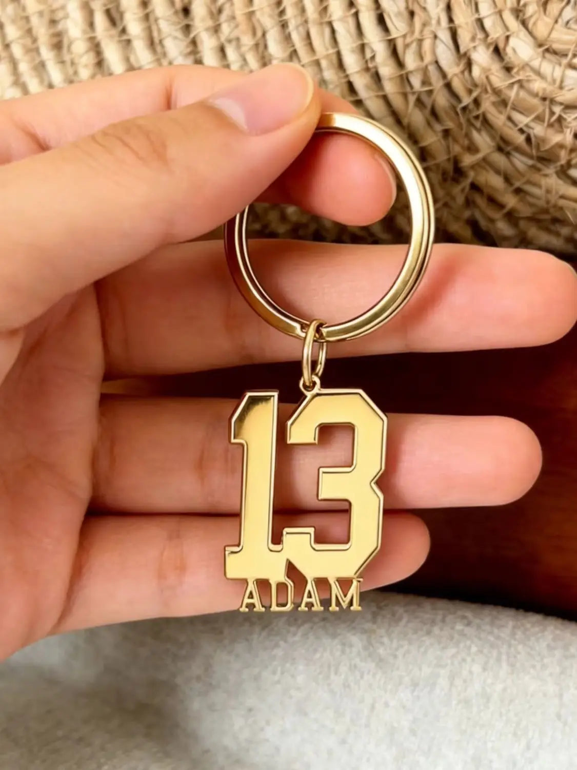 Gold-colored metal custom number and name keychain featuring the number 13 and the name Adam in a bold blocky font.