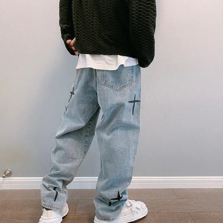 Pantalon cargo en jean à jambes larges à effet délavé clair avec broderie croisée noire, sur les cuisses et les poignets.