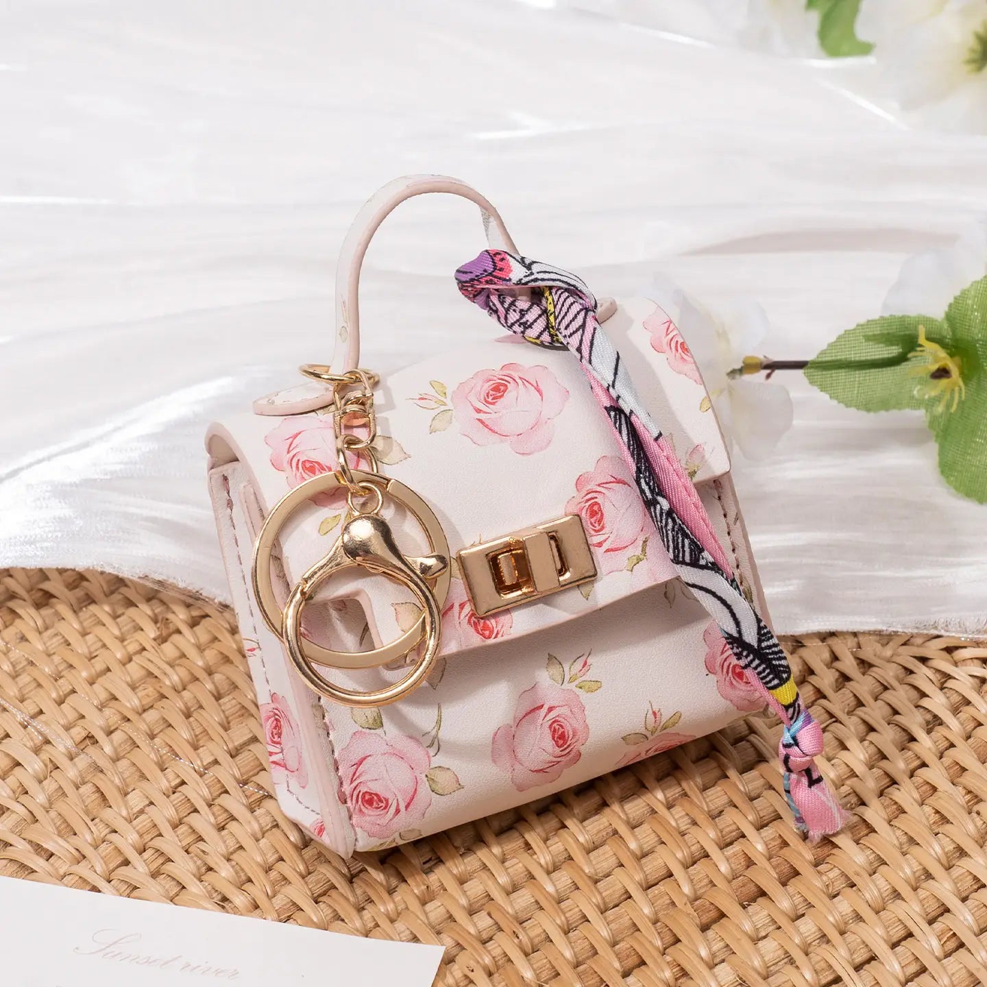 Miniature handbag keychain featuring a delicate pink floral-patterned mini handbag with gold-tone hardware and a matching silk scarf ribbon tie.