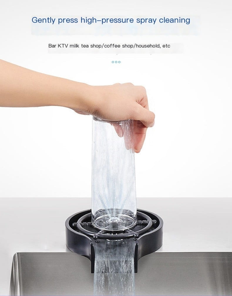 Ein transparenter zylindrischer Glasbecher, der von einer Hand über einem schwarzen Kunststoff-Tropfauffangbehälter in einem Hochdruck-automatischen Becherwascher gold gehalten wird.