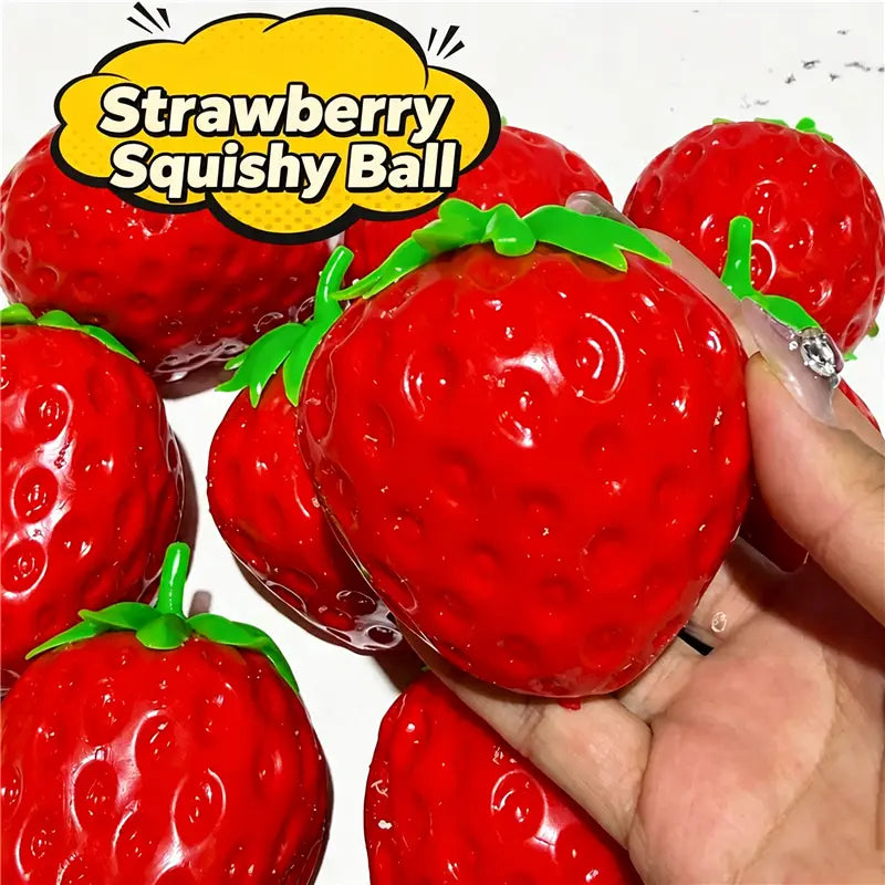 Un jouet sensoriel de type balle anti-stress en forme de fraise rouge, brillant, avec des feuilles en plastique vert et une surface texturée, tenu dans la main.