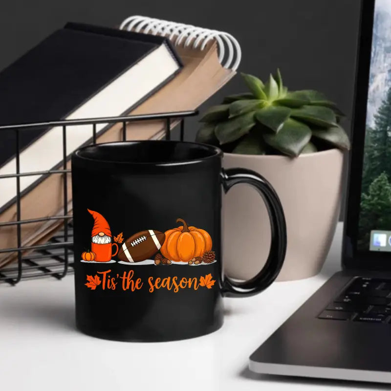 Black ceramic Easter egg coffee mug featuring a festive orange and white illustration of a gnome football pumpkin and the phrase tis the season surrounded by autumn leaves.