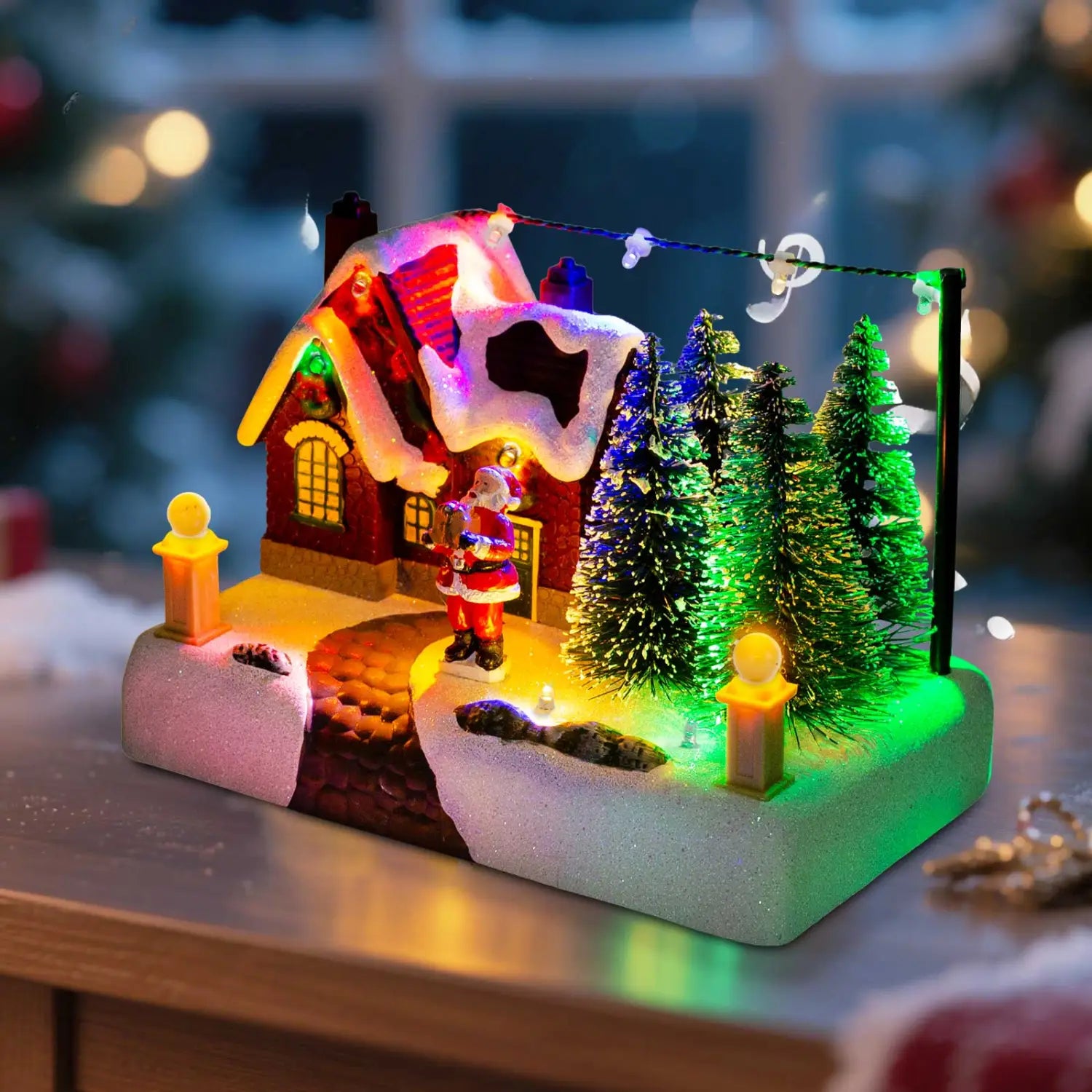 サンタと雪を備えたLEDクリスマスビレッジの家。雪の積もった屋根と光る窓のある、装いのある赤い照明付きの家が、ミニチュアのホリデーシーンで輝いている様子。