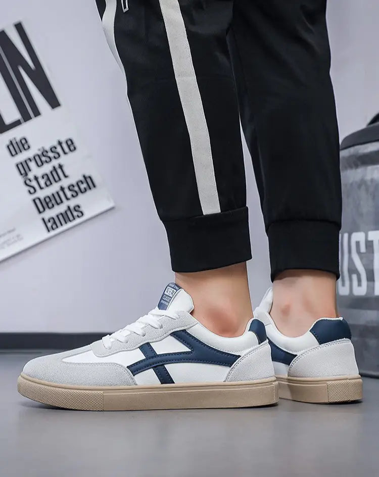 Sneakers décontractées pour hommes, chaussures de marche légères, en blanc et bleu marine, avec un bout texturé en gris, semelle extérieure en caoutchouc beige et design classique à rayures croisées.