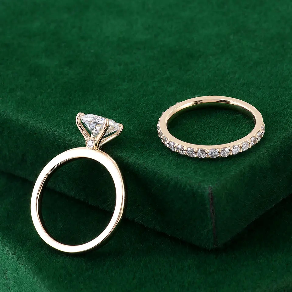 Une paire de bagues élégantes, tons or, pour ensemble de bague de fiançailles en diamant de laboratoire ovale, l’une avec un diamant central proéminent et des pierres d’accent plus petites, et l’autre avec une ligne continue de minuscules diamants.