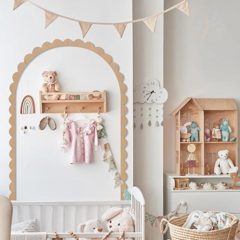 A soft pink baby dress with delicate ruffled sleeves and button-front design hanging on a wooden rack in a cozy nursery featuring scalloped wood wall arch diy decor trim.