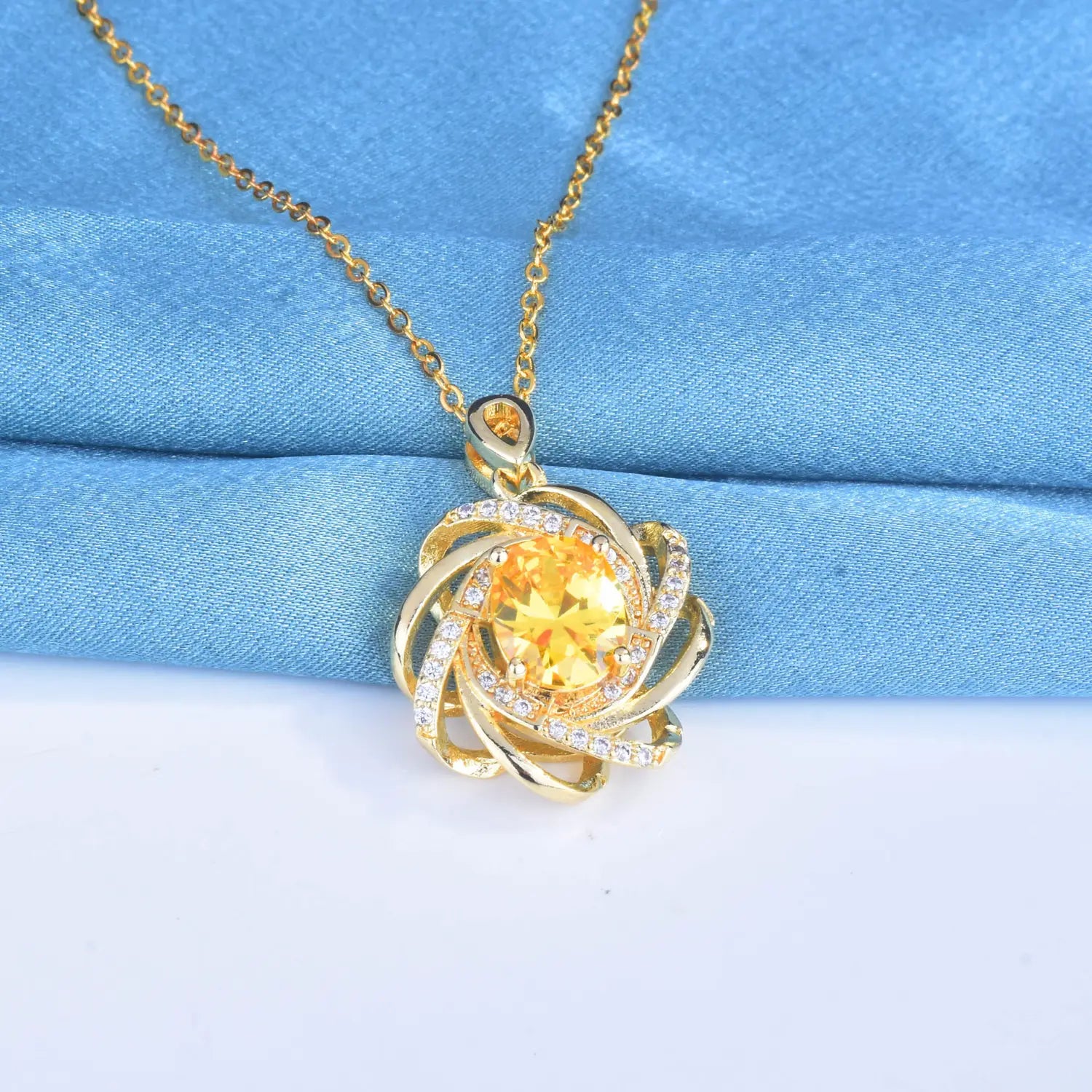 Collier pendentif moulin à vent en citrine doré comportant une pierre jaune centrale entourée de bandes dorées tourbillonnantes et de petites pierres transparentes.