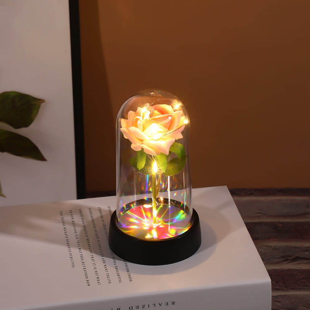 Une rose d’un ton pêche luisant enfermée dans un dôme en verre transparent avec des reflets de lumière arc-en-ciel sur la base dans le cadeau de fleur lumineux en dôme de rose éternelle.