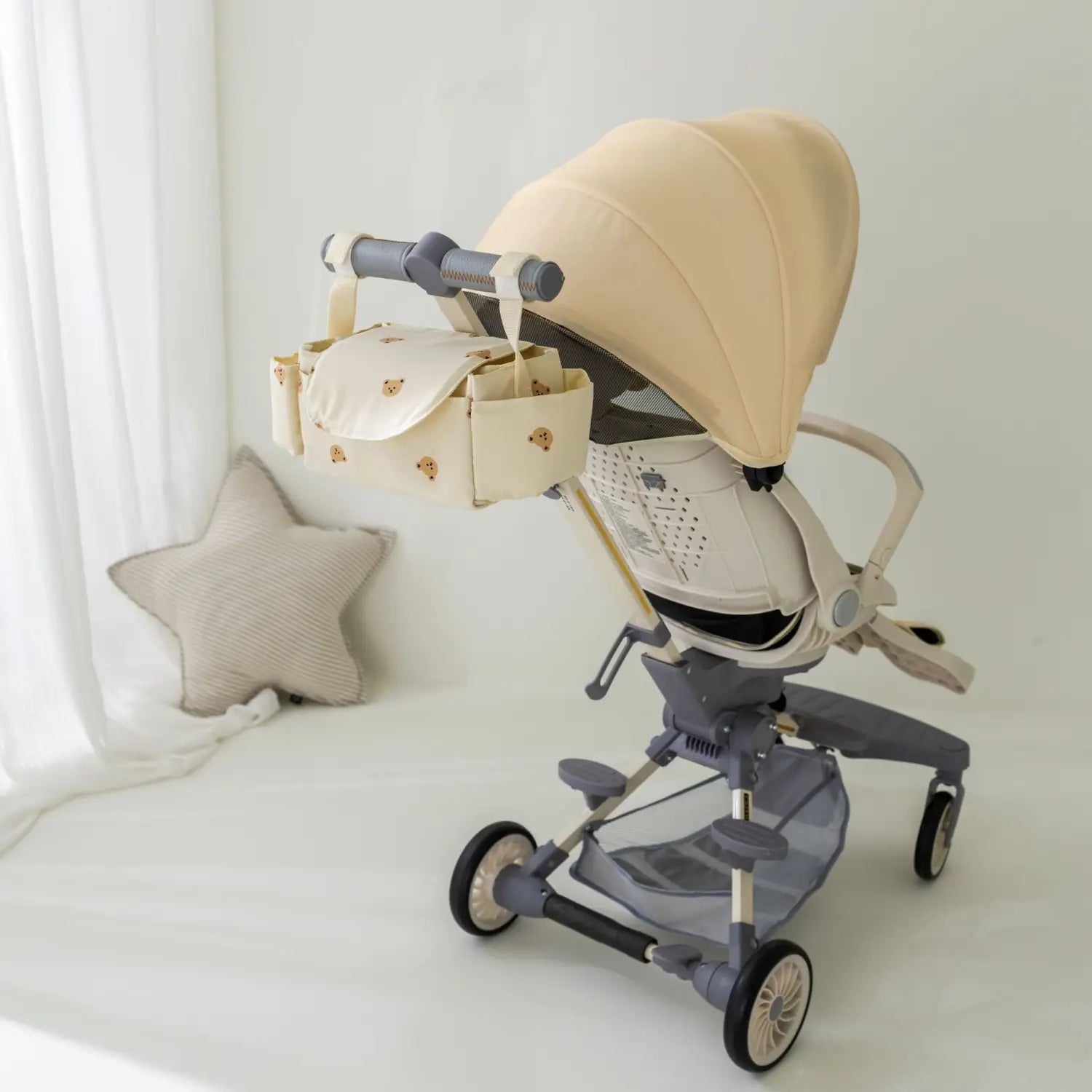 グレーの金属フレームと、コーディネートしたカバー（キャノピー）を備えたベージュのベビーカー。ハンドルバーに取り付ける、クマのデザインのコーディネートされたベビーカーオーガナイザーバッグ付き。