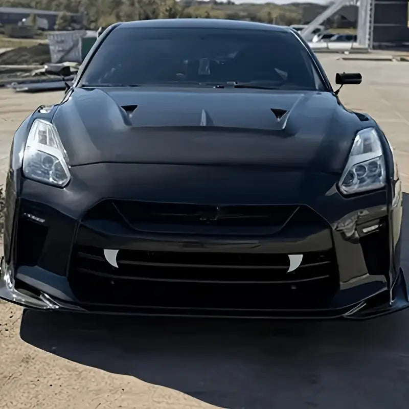 Schwarzer, matt ausgeführter Nissan GT-R mit aggressivem aerodynamischem Design und markantem Frontgrill, mit Halloween-Vampirzahn-Autotaufklebern aus Kunststoff-Monsterfängen.