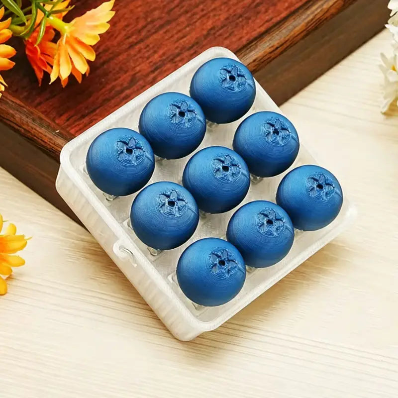 neuf jouets d’apaisement « fidget » en forme de baies, imprimés en 3D et de couleur bleu brillant, disposés dans un petit contenant en forme d’œuf en plastique blanc, conçus pour soulager le stress.