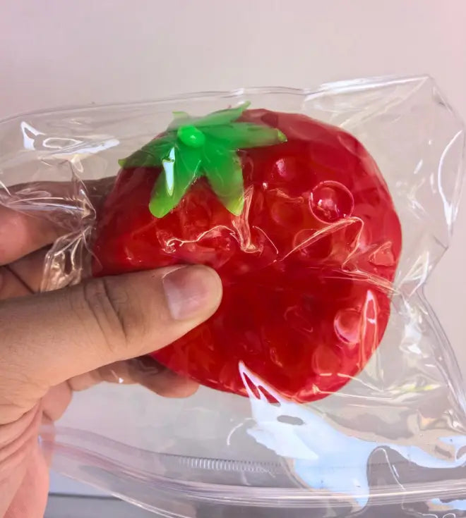 une fraise translucide rouge vif, en forme de fromage, remplie de gel, avec un dessus vert feuillu brillant, conçue pour soulager le stress et apaiser le stress lié au jouet