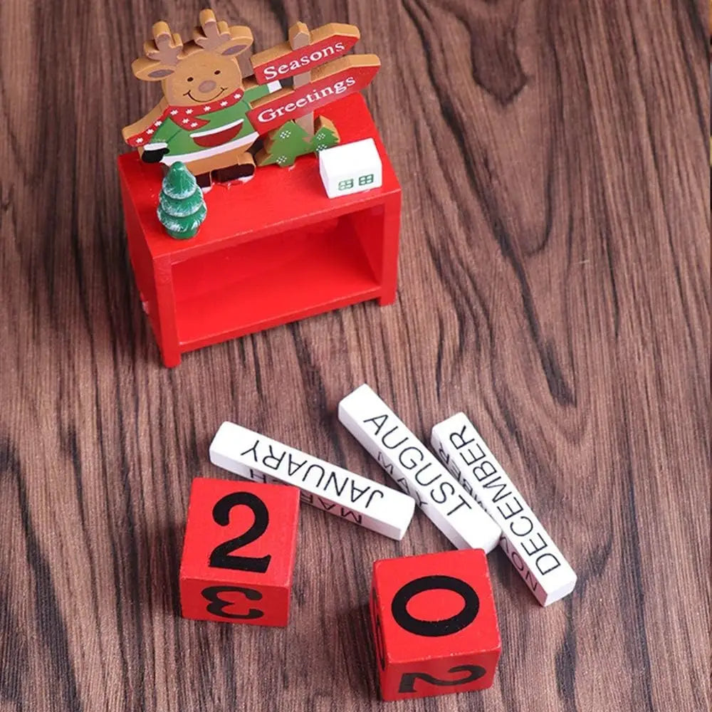 Red wooden Christmas countdown calendar blocks with carved reindeer figure in green and red sweater and seasons greetings sign, featuring miniature tree and white month blocks.