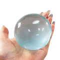 A translucent light blue gel ball stress toy filled with coconut oil held in a hand for squeezing and stress relief