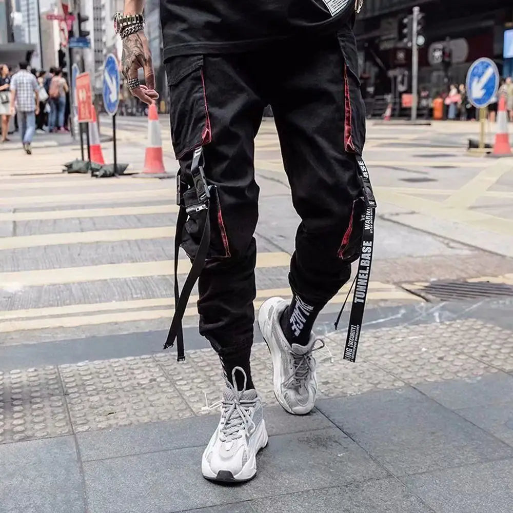 Pantalon cargo joggers streetwear pour hommes en tissu tactique noir, avec bordure rouge et bretelles de marque de type tunnel.