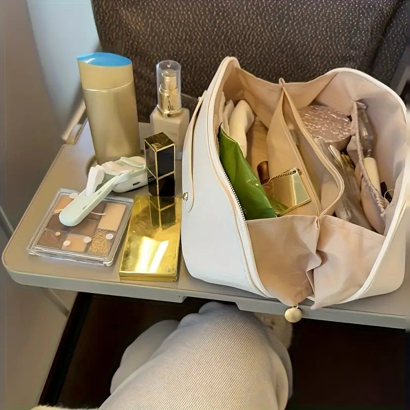 Beige Stoff-Reise-Make-up-Tasche und Kosmetikorganizer aus weißem Stoff mit beiger Innenseite und einem kleinen perlenartigen Anhänger am Reißverschluss-Zieher.