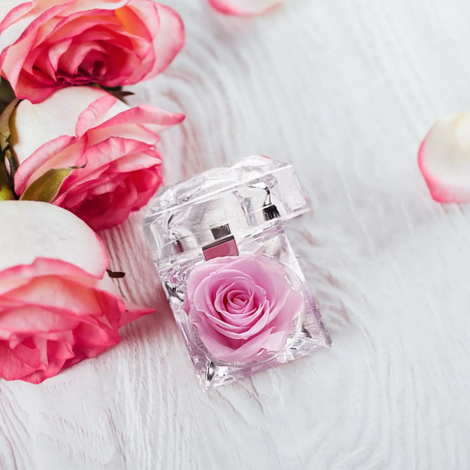 A clear square-shaped perfume bottle with a delicate pink preserved rose inside from the preserved rose crystal gift box eternal flower collection.