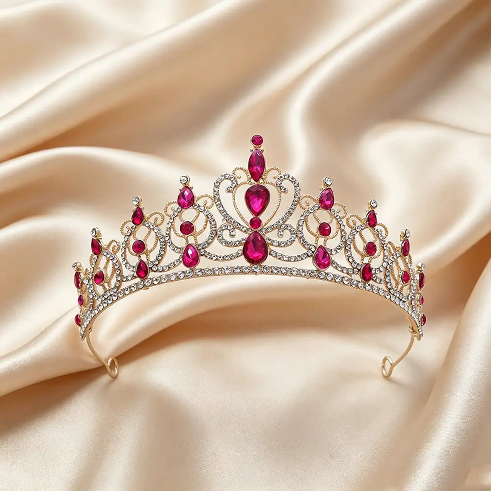 Une couronne de diadème baroque en strass doré étincelante, ornée de pierres précieuses vibrantes en forme de goutte rouge et de cristaux transparents, disposés sur un fond de satin doux.
