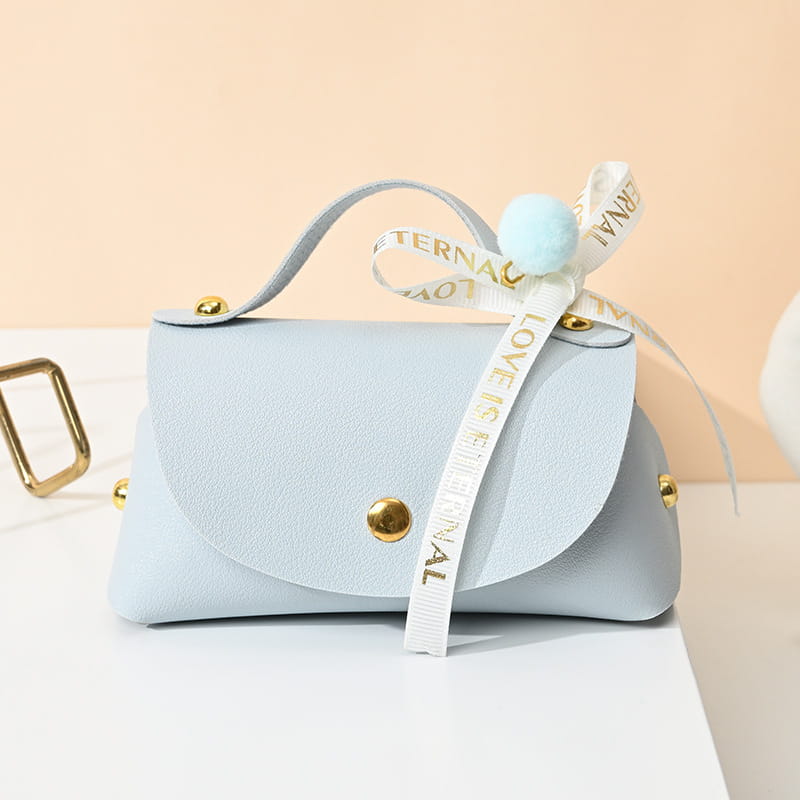Mini sac à main en faux cuir bleu pastel avec quincaillerie ton or et un ruban blanc décoratif noué en forme de nœud, portant la phrase « l’amour est éternel », conçu comme sac cadeau de mariage en cuir.