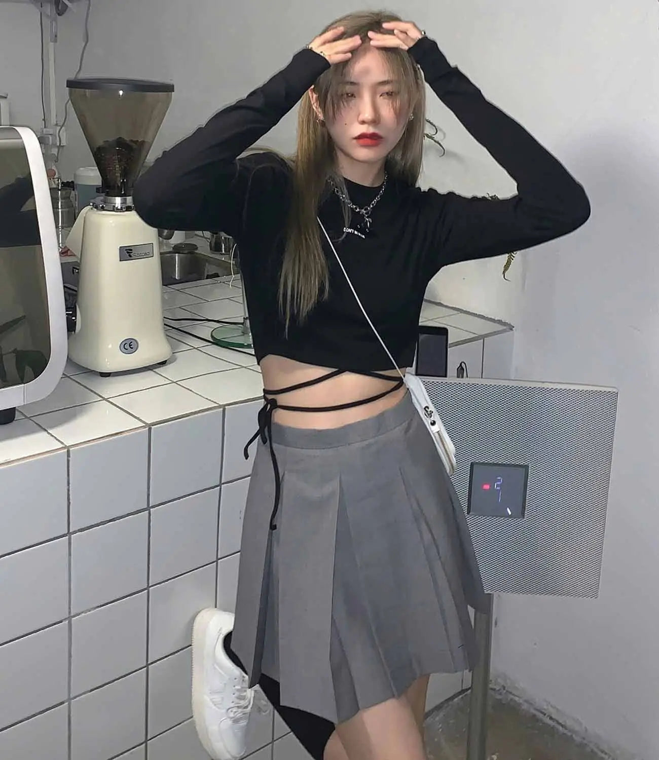 Damen-Langarm-Crisscross-Crop-Top, kombiniert mit einem grauen plissierten Rock mit schwarzen Seitenpaneelen und Front-Bindungsdetail.