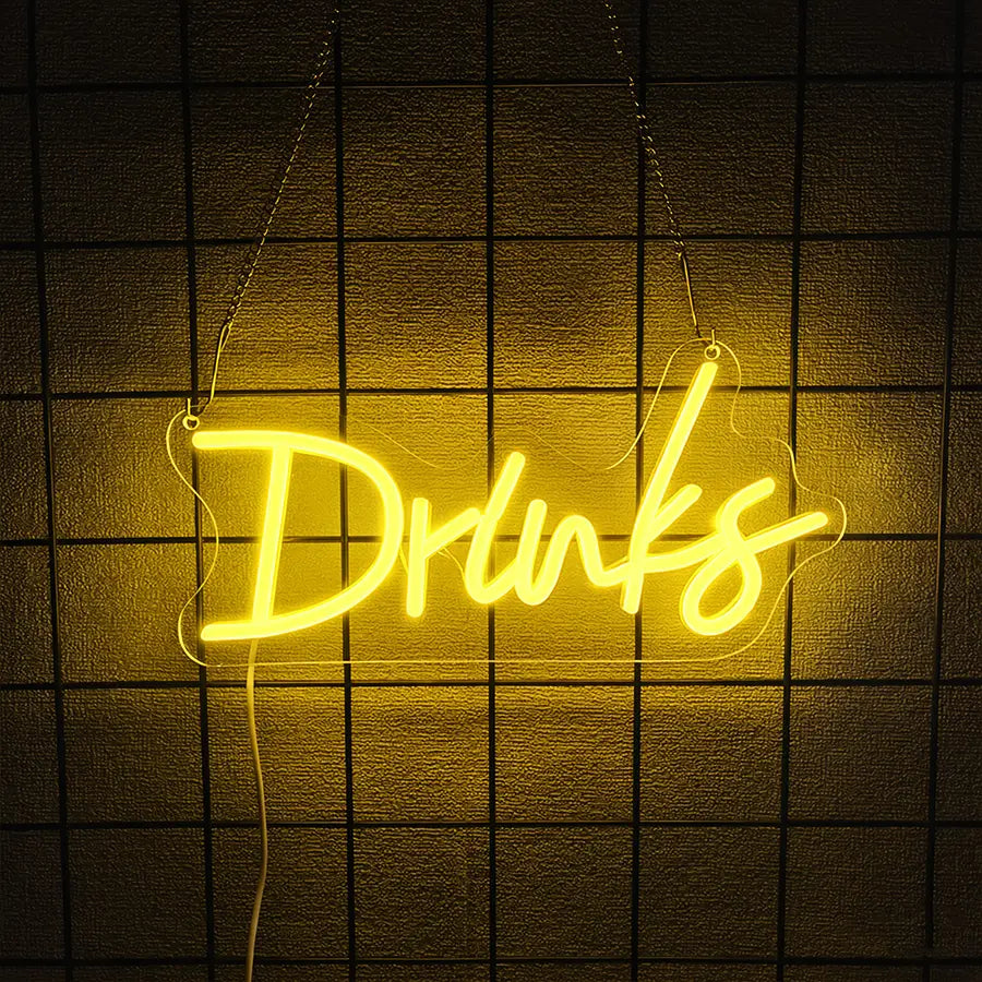 une enseigne au néon jaune lumineuse formée comme le mot « drinks » dans un style cursif à LED, suspendue sur un mur sombre à motif de grille, en tant que décoration murale pour enseigne au néon