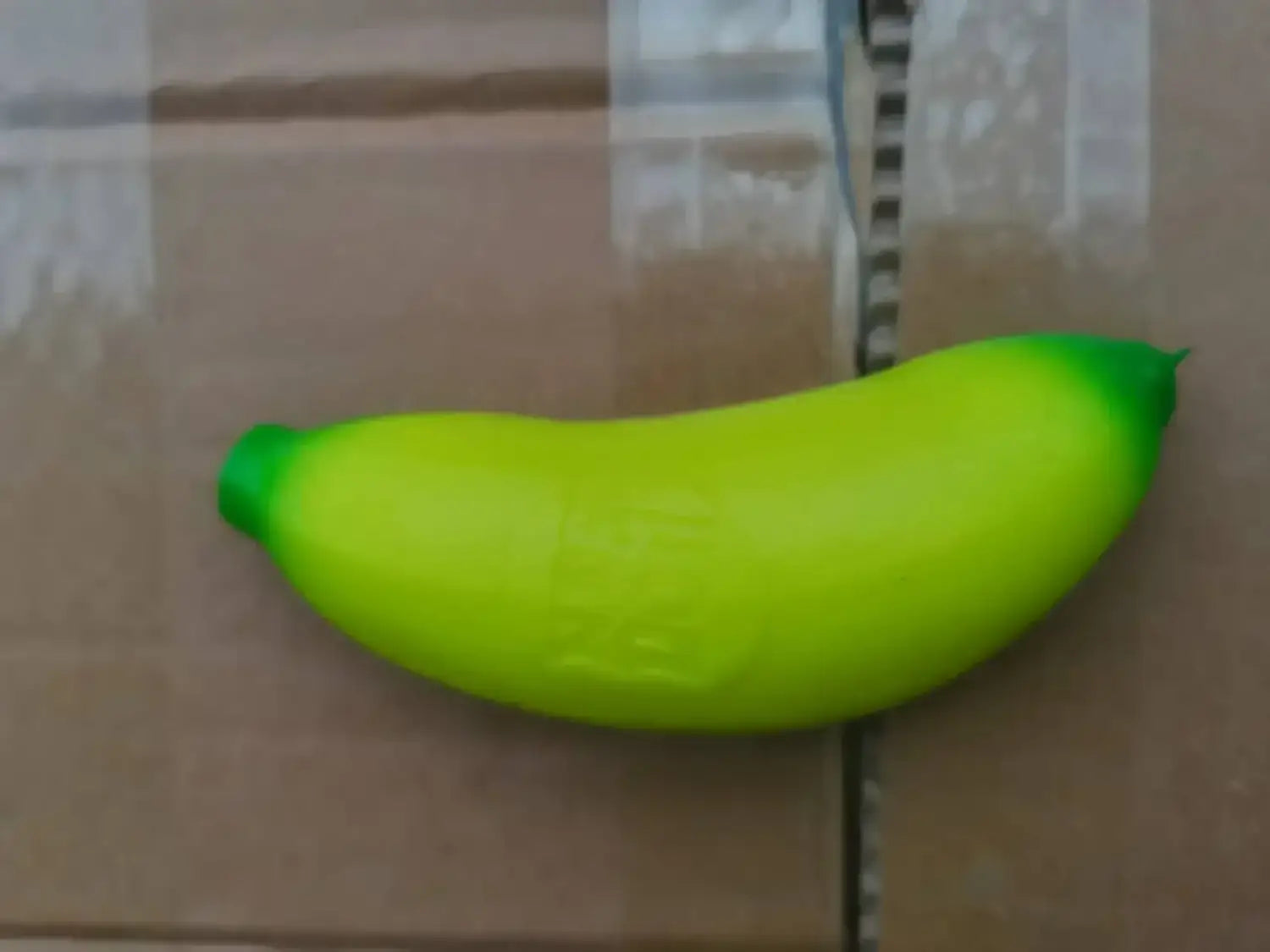 Ein leuchtend limettengrünes, bananenförmiges quetschbares Spielzeug mit glänzender Kunststoffoberfläche aus dem Erdbeere-Orange-Banane-Stressabbau-Set.