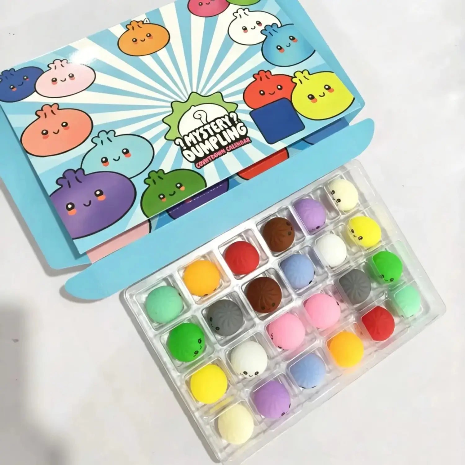 Ein farbenfroher Adventskalender „Dumpling Squishies“ im Kawaii-Thema mit einer blauen Box mit Cartoon-Knödelsymbolen und einer transparenten Schale, die 24 weiche Pastell- und lebendige Silikon-Knödel-Squishies enthält.