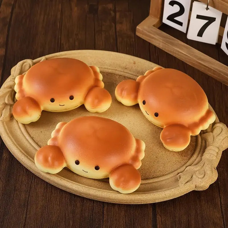 three golden-brown plush crab-shaped slow rising toast fidget toys with smiling faces on a rustic beige tray designed for daily stress relief.