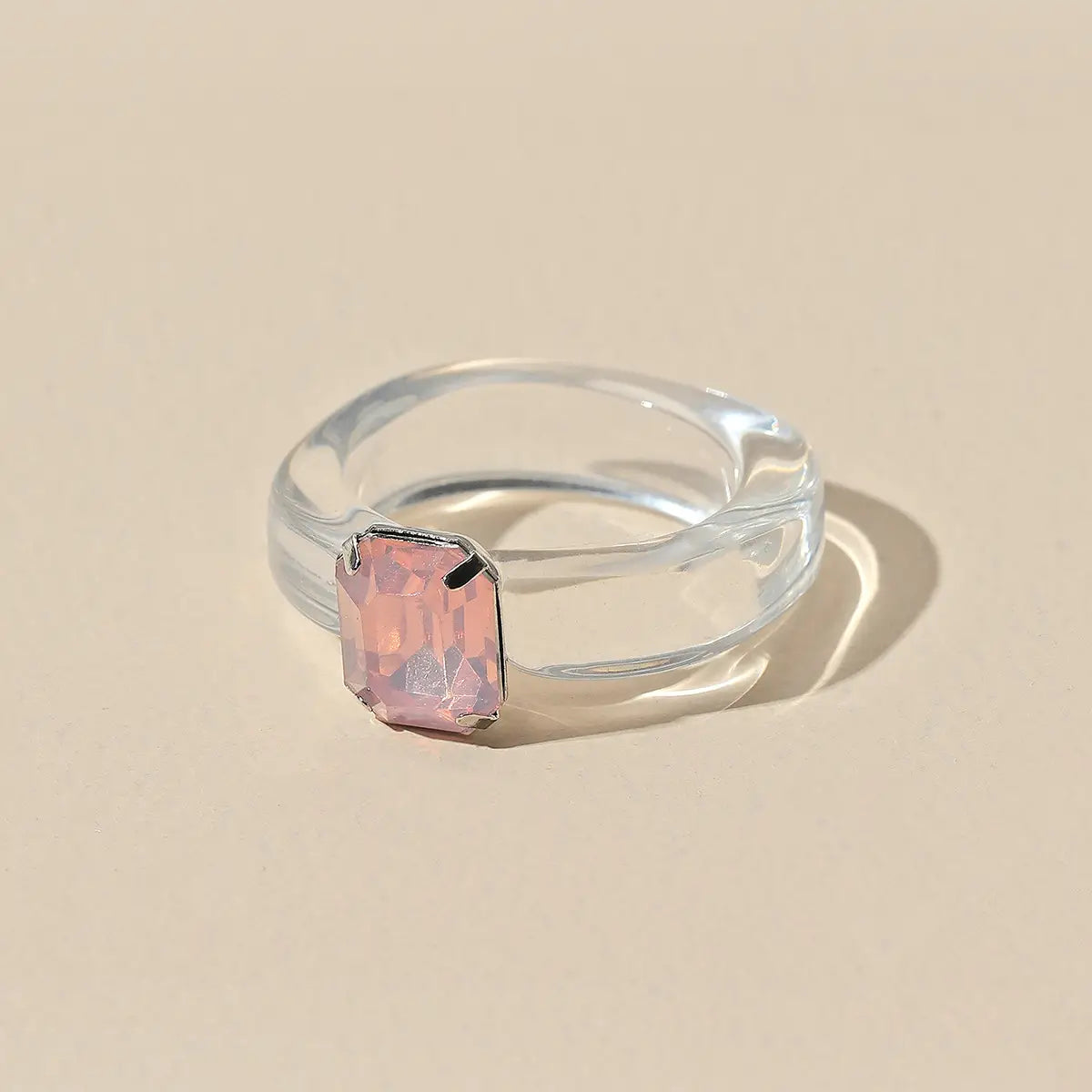 A colorful resin crystal geometric ring for women featuring a translucent clear slightly curved band and a rectangular pink gemstone set in a silver-toned bezel.