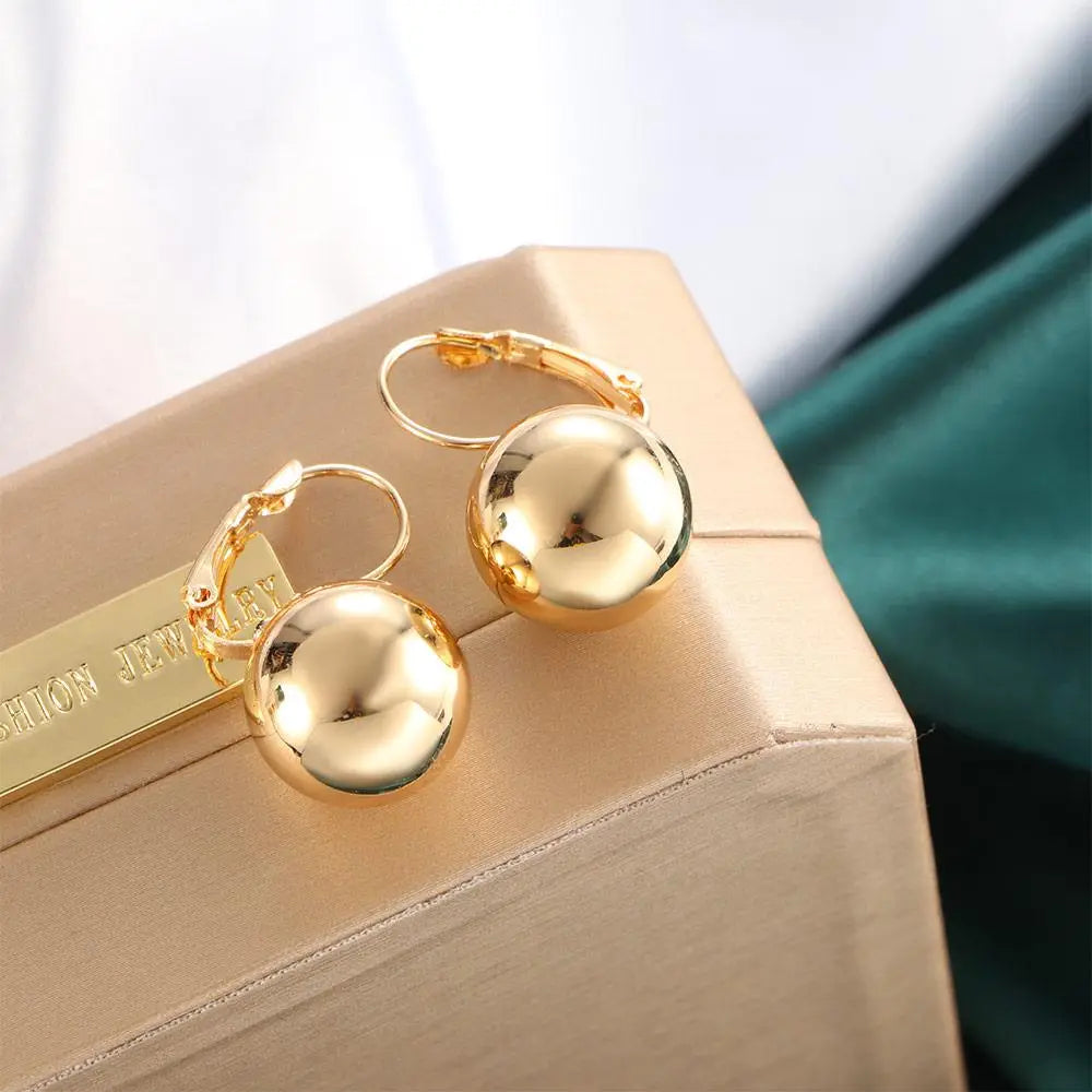 Se muestran pendientes de aro de oro con encantos esféricos pulidos en oro rosa y plata.
