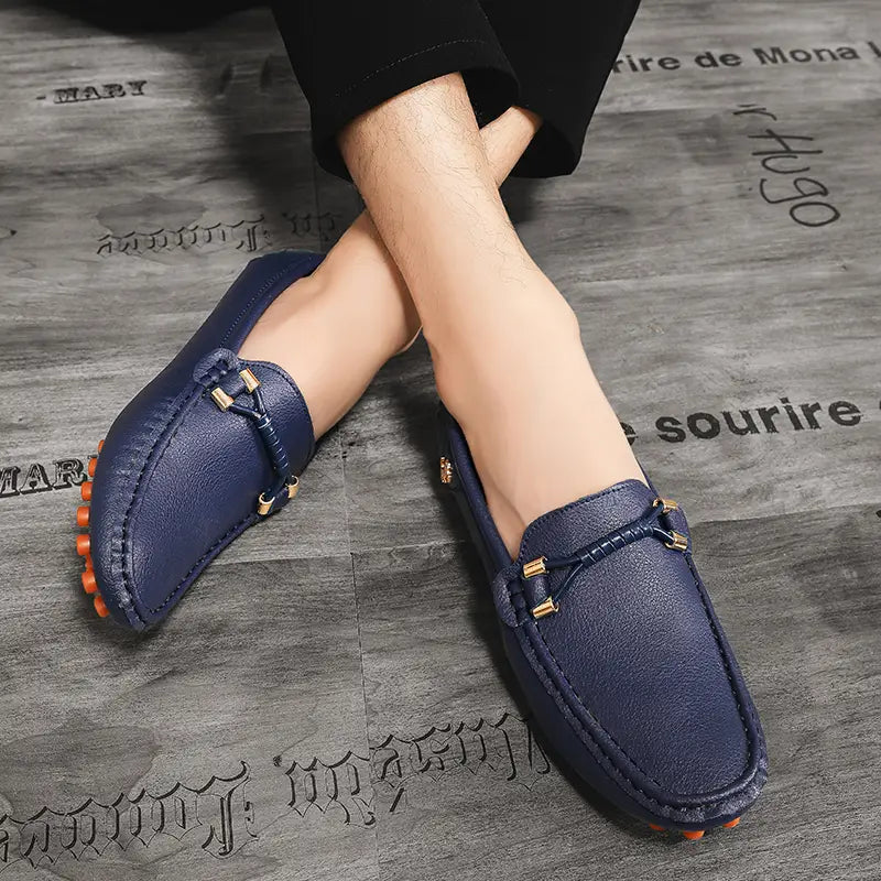 Chaussures à enfiler habillées en cuir bleu marine pour hommes, se portant sans effort avec des chaussures décontractées, avec des accents métalliques ton or et des semelles en caoutchouc orange.