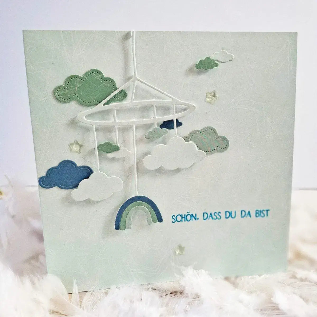 Oster-Ei-Hasen-Babyschneidvorlagen mit einem zarten, dreidimensionalen Babymobile, gefertigt aus geschichteten Papier-Ausschnitten in sanftem Mintgrün und Weiß, mit einem dezenten Regenbogenbogen am unteren Rand.