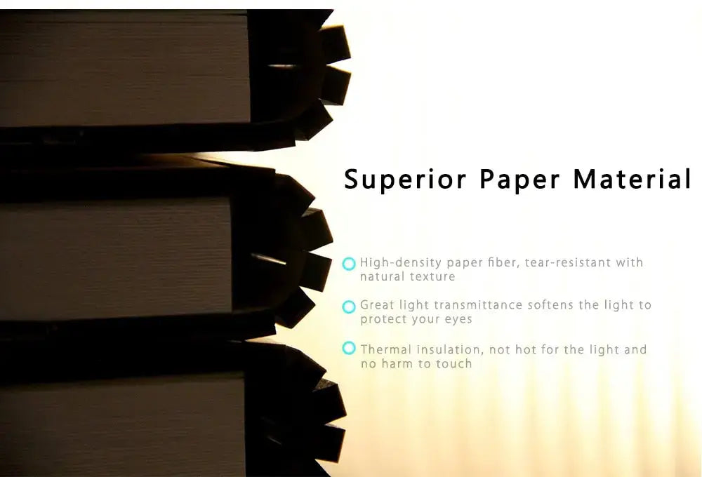Pila de libros gruesos de tapa oscura con lomos de papel texturizado, colocada junto a una lámpara de mesa recargable con luz LED plegable con forma de libro.