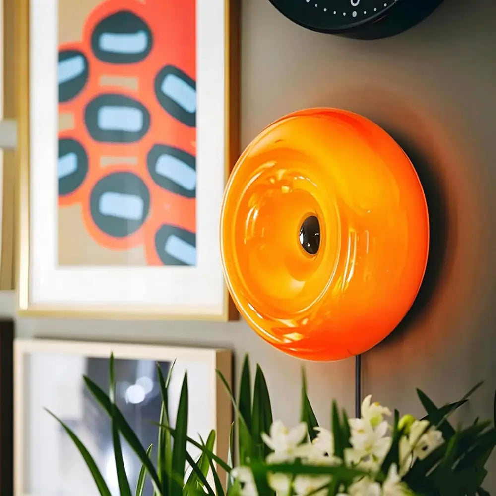 Luminaire mural en acrylique orange éclatant, présentant un design circulaire en verre laqué évoquant un œil, avec luminosité réglable.