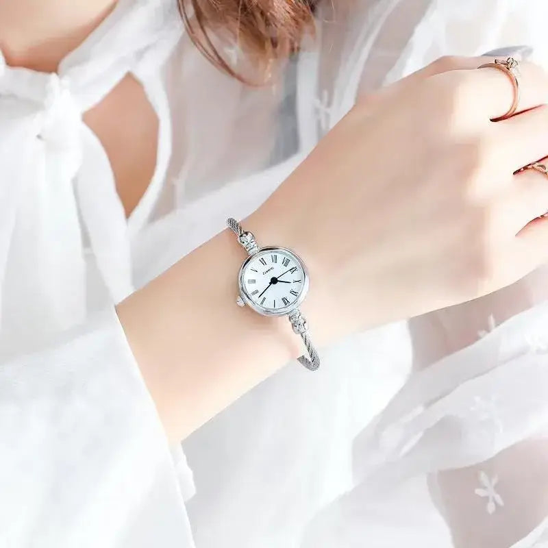 Women stainless steel quartz bangle watch featuring a silver-toned bracelet-style design with a round white dial, roman numerals, and an ornate braided metal band.