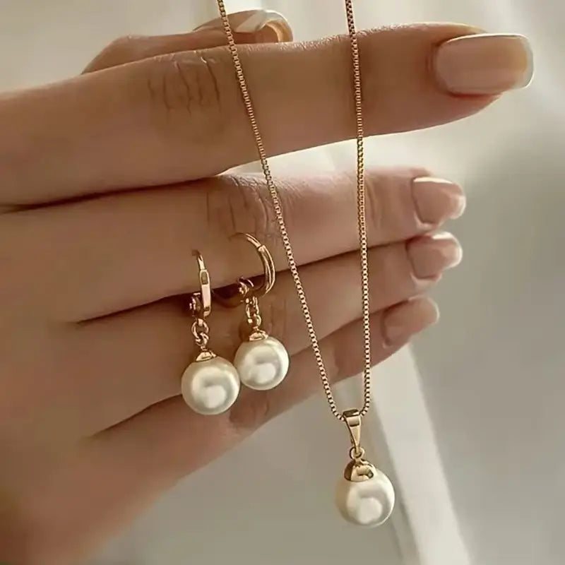 Un ensemble délicat de bijoux en perles ton or, comprenant un collier à pendentif de forme goutte et des boucles d’oreilles créoles assorties, avec des perles plus petites.