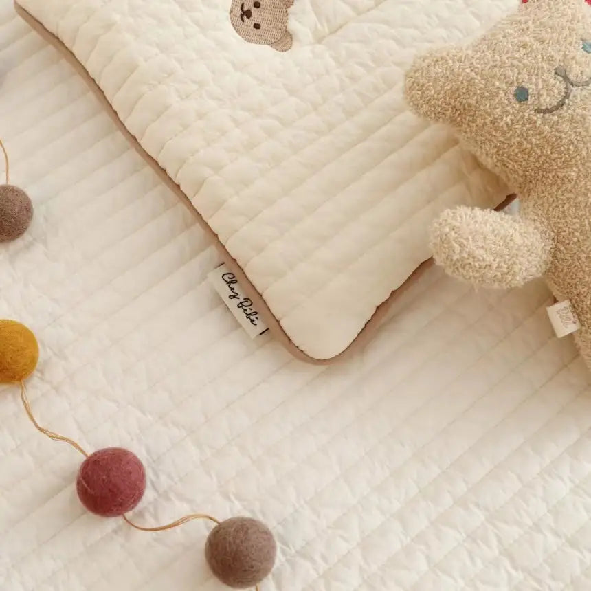 刺繍入りのクマの顔と、やわらかなふわふわの質感を備えたクリーム色のキルティングコットンのベビーピロー。