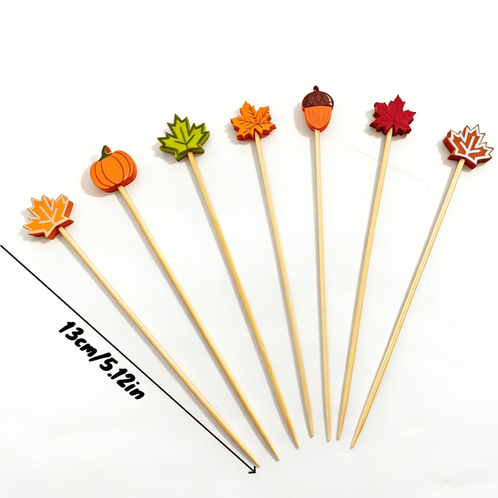 Set of six bamboo food skewers topped with colorful autumn-themed wooden cutouts shaped like pumpkins leaves and acorns.