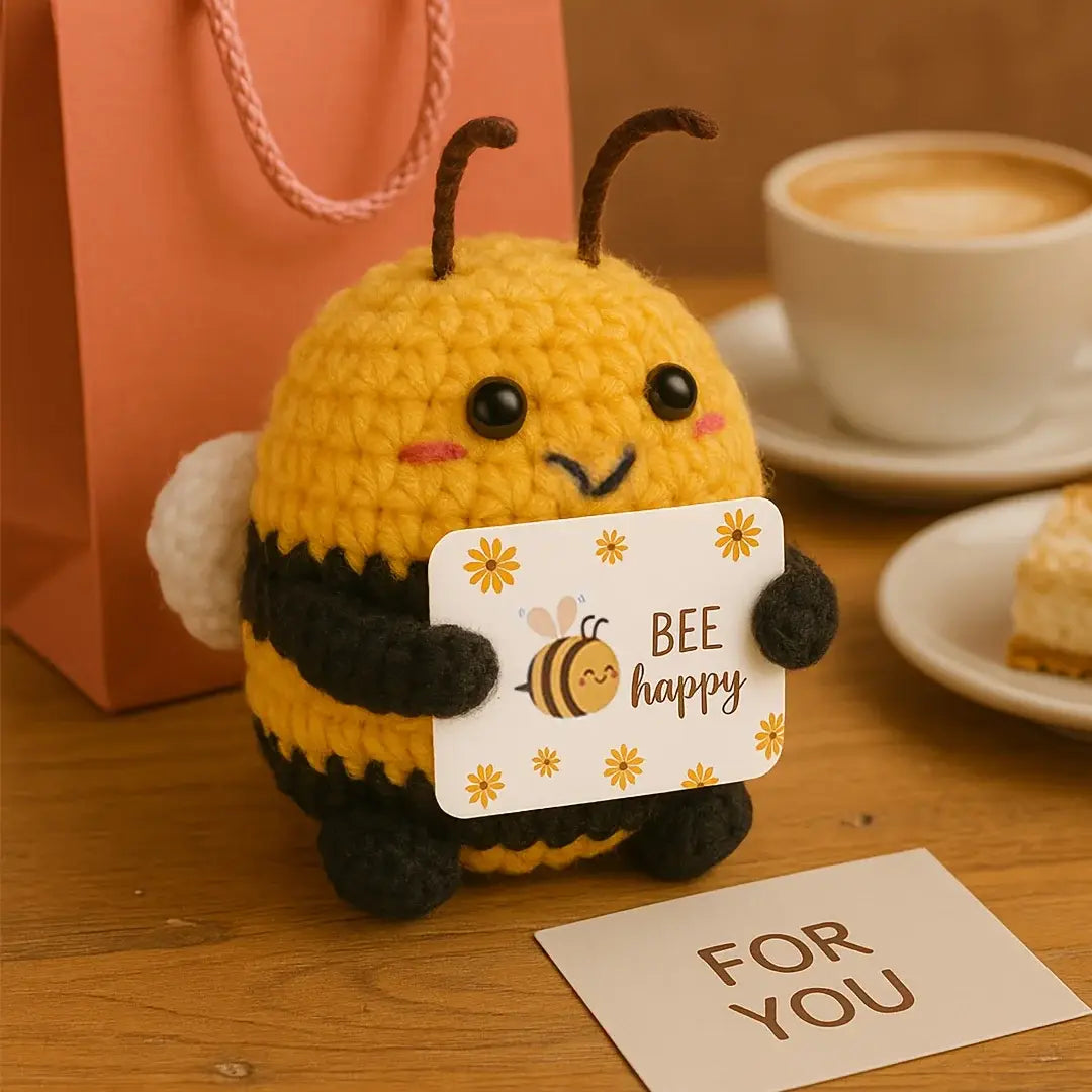 peluche de abeja tejido a ganchillo color amarillo y negro que sostiene una tarjeta de abeja feliz, presentada como llavero y accesorio para bolso de abeja positiva tejido a ganchillo.
